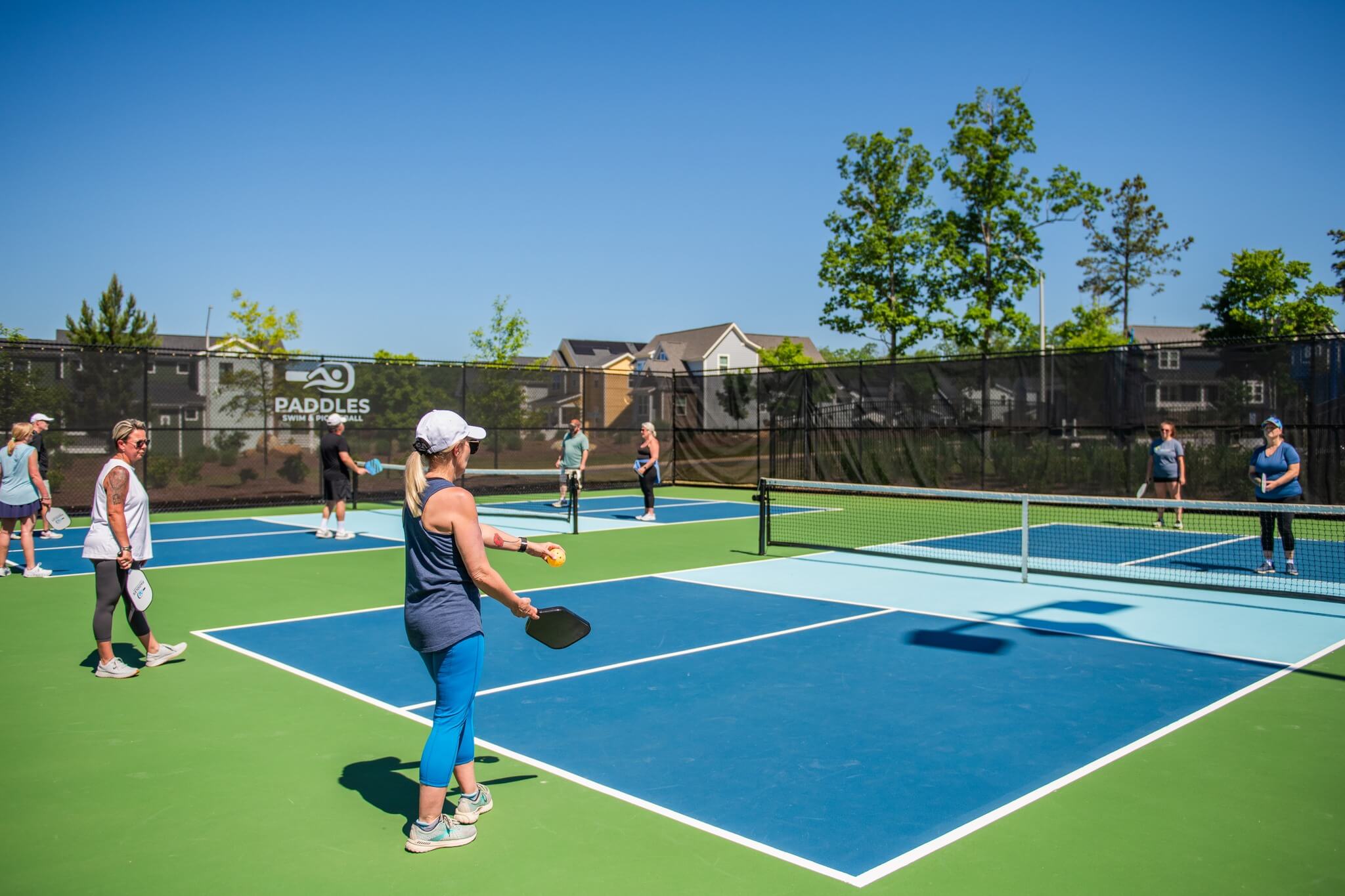 Beginner and intermediate pickleball players on green and blue court.